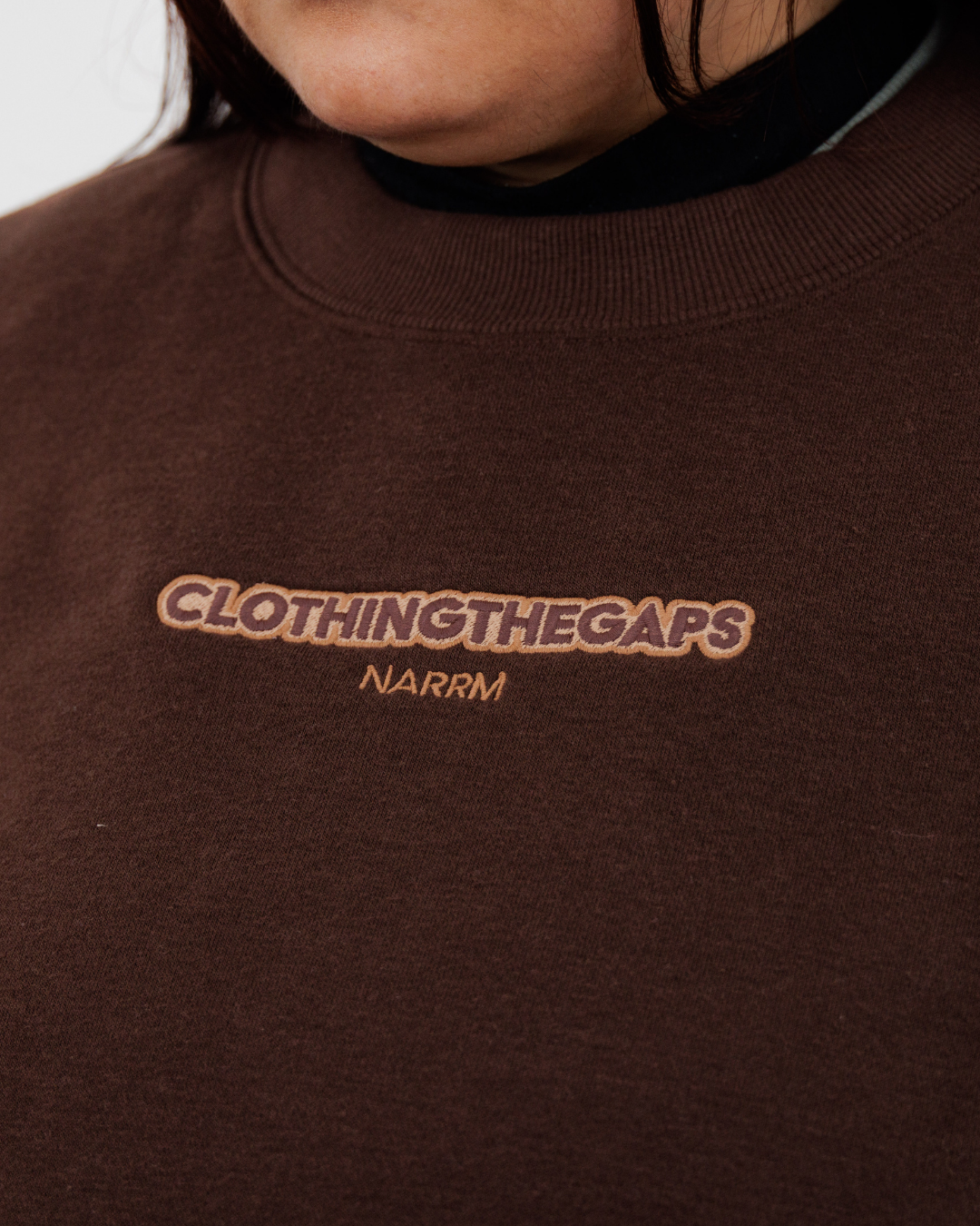 Clothing The Gaps. Chocolate Crew Jumper. Brown chocolate crew neck jumper. With tonal lighter brown 'Clothing the gaps' and the word 'Narrm' embroidered on the front of crewneck.' Wear your values' is also embroidered small on the back of the crew with the same light brown tonal colour. The wrist cuffs of the crew have a woven tonal brown aboriginal flag on them. 