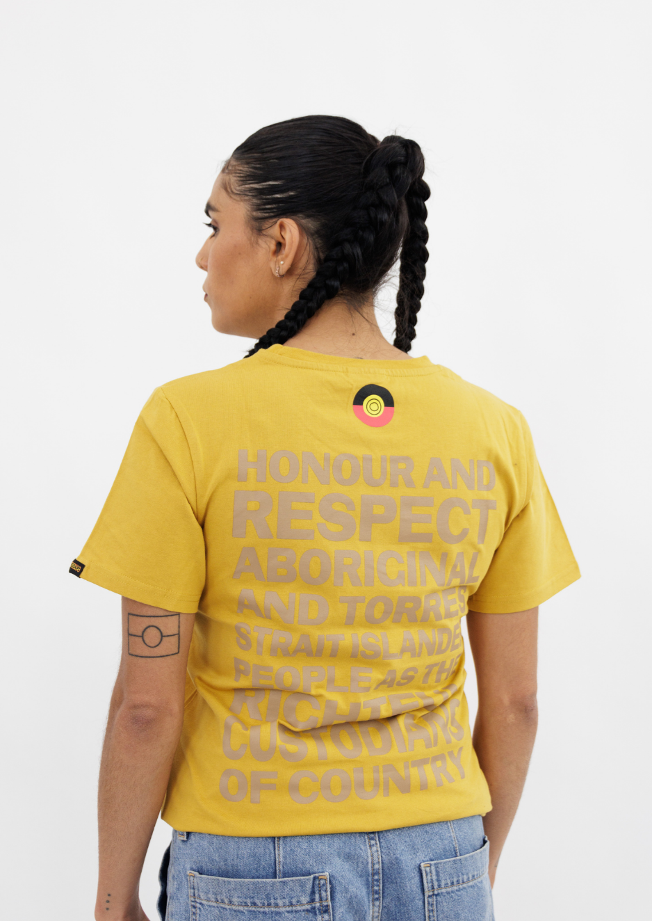 Clothing The Gaps. Kids Mustard Honour Country Tee. Mustard yellow t-shirt with screen printed bold capital text 'Honour and respect Aboriginal and Torres Strait Islander people as the rightful custodians of country.' The word 'Honour country' on the front in the same text and contrasting colour.