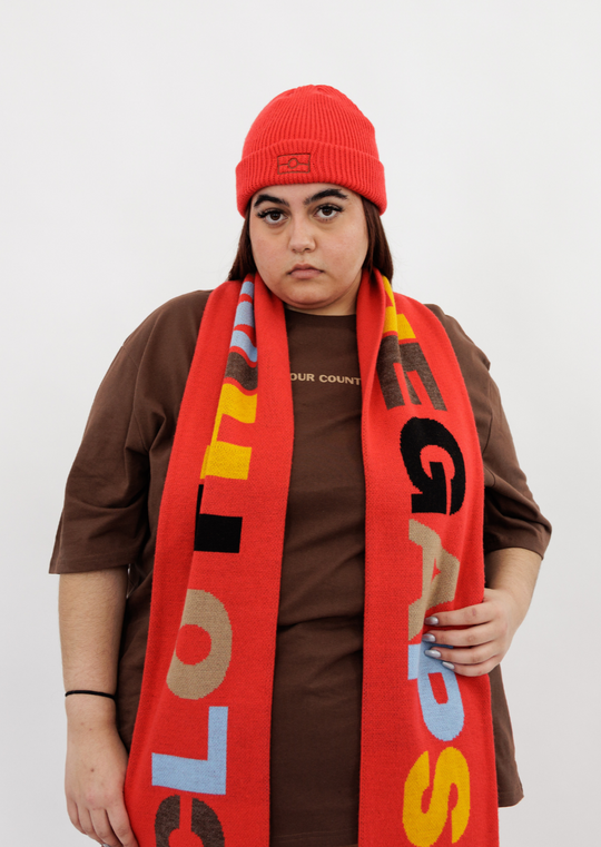 Clothing the gaps. Red CTG Scarf. Long thick red scarf with big letters reading 'Clothing the gaps' with letters in alternating colours of light blue, cream, brown, yellow and black. Red and light blue at ends of scarf.