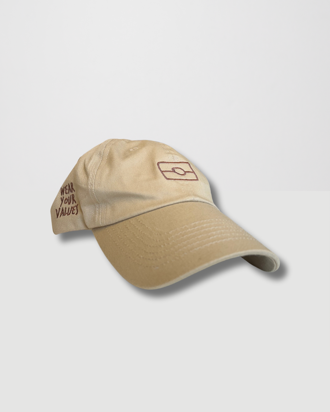 Clothing The Gaps. The OG 2.0 Cap. Beige adjustable cap. With embroidered brown outline of aboriginal flag on front. 'Wear your values' text embroidered on side of cap in same brown colour. Clothing The Gaps embroidered on back in brown stitching. Adjustable clip strap on back with silver clip featuring Clothing The Gaps logo.