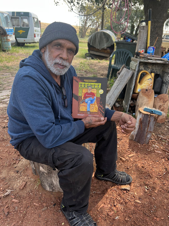 Clothing The Gaps. 1000 piece Puzzle of Aboriginal man with traditional face paint wearing a red sovereignty t-shirt on a yellow possum skin cloak chair. With a brown and green aboriginal style background using dots lines to tell story. Artwork by Norm Yakaduna.