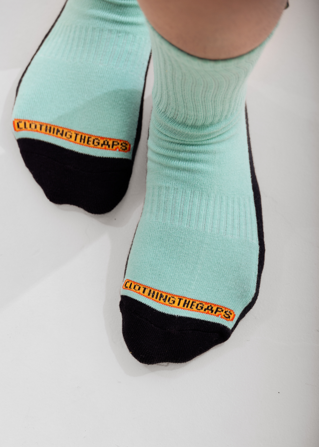 Light blue socks with black toes and heels, featuring a Clothing The Gaps brand logo on the top, worn by a person.