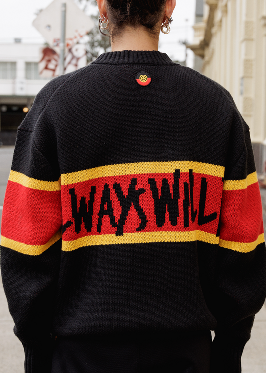 Person wearing a black sweater with red and yellow stripes and 'ALWAYS WILL BE' text on the back, standing on a street. Clothing The Gaps Knit