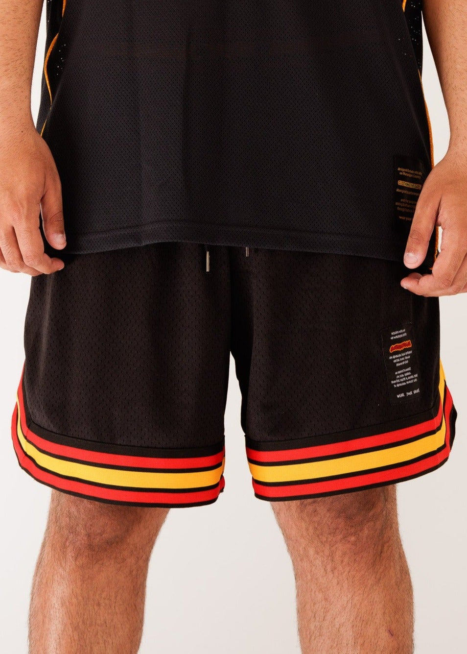 Clothing The Gaps. Blak Basketball Shorts. Retro look with red, black and yellow stripes around bottom of shorts, on pocket opening and around waist band. Rest of the shorts are a black mesh material. Has a elastic waist, black drawstrings, deep pockets and clothing the gaps patch on corner of left leg.