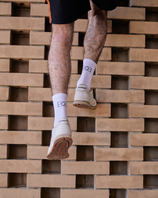 Clothing The Gaps. Long black socks with white Aboriginal flag outline on back. Yellow on heel of socks. Red on toes of socks. Clothing The Gaps written above red section just going over toes.