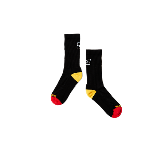 Clothing The Gaps. Long black socks with white Aboriginal flag outline on back. Yellow on heel of socks. Red on toes of socks. Clothing The Gaps written above red section just going over toes.