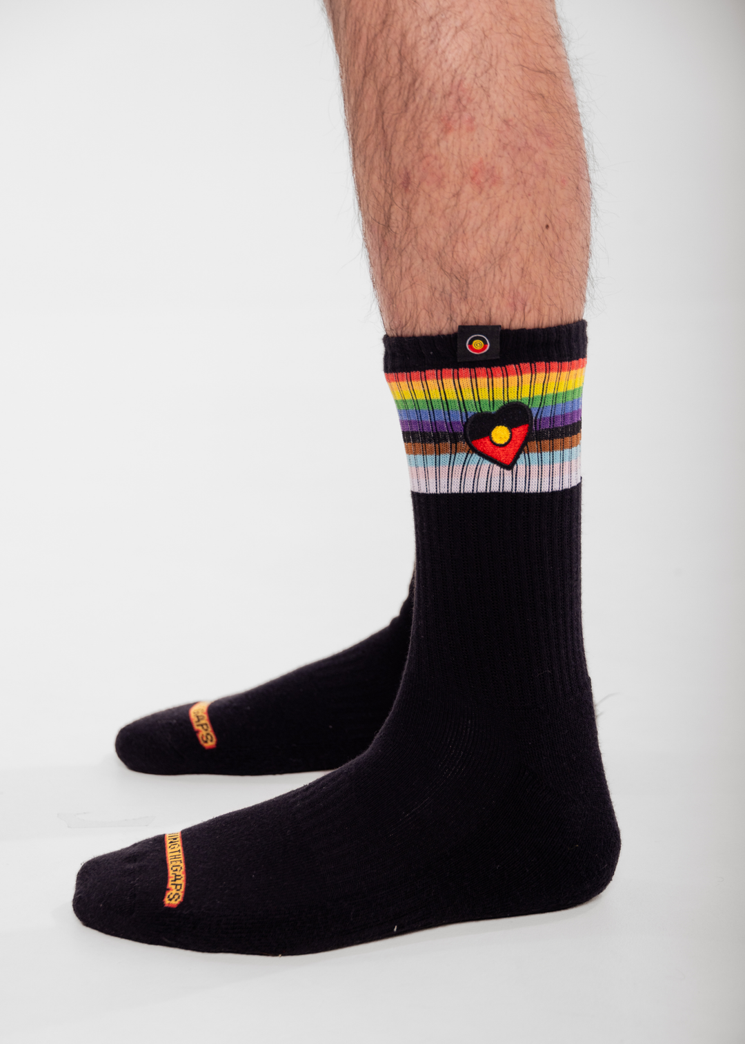 Black socks with rainbow and  Aboriginal flag heart design on a white background