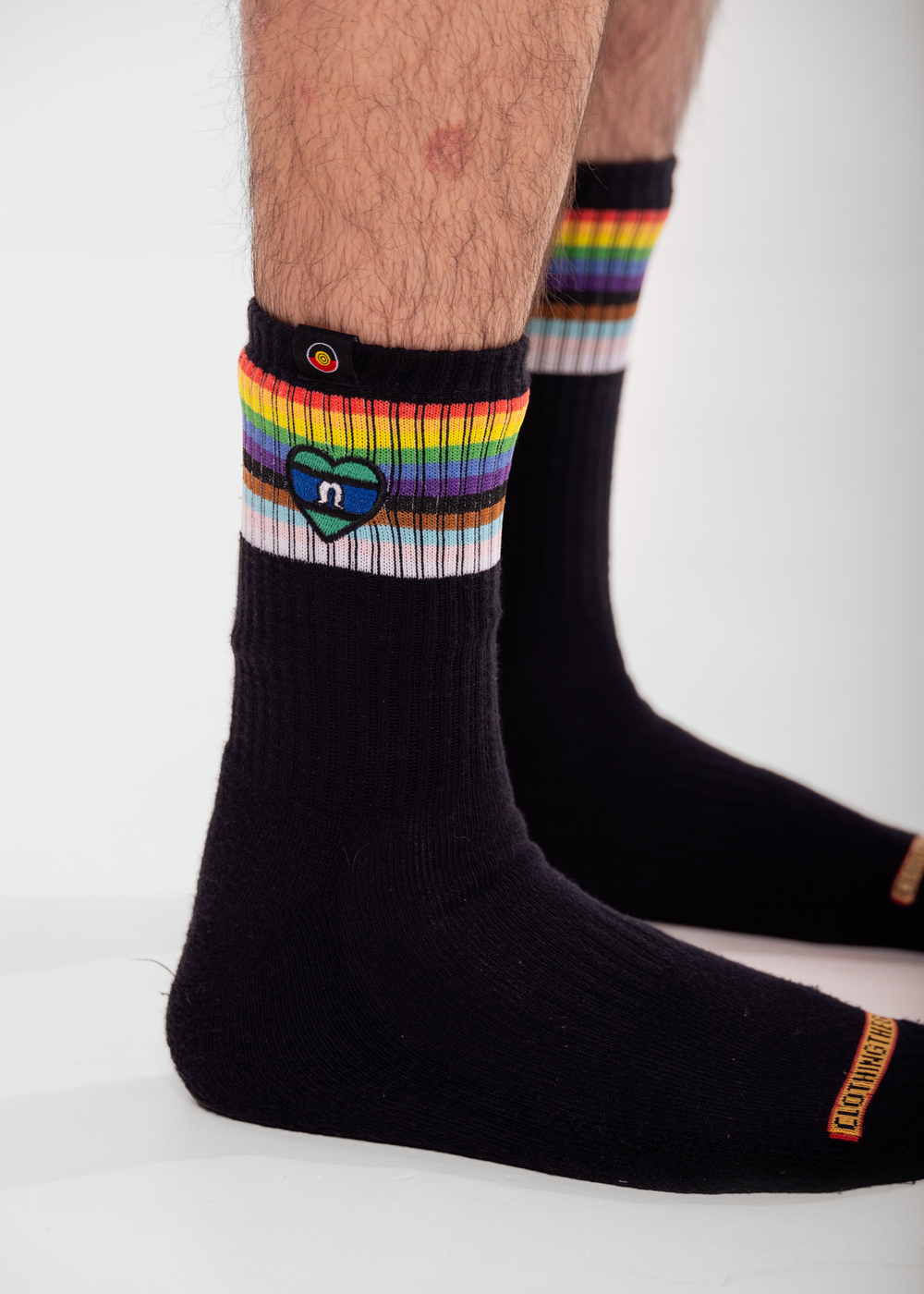 Black socks with rainbow striped cuffs and a heart logo on a white background TSI heart