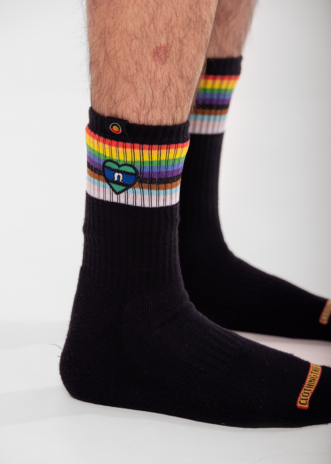 Black socks with rainbow striped cuffs and a heart logo on a white background TSI heart