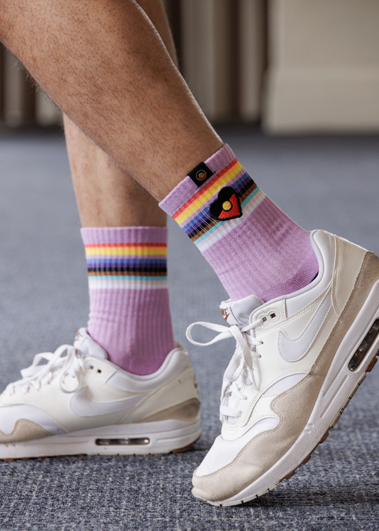 Person wearing purple socks with rainbow stripes and white sneakers on a gray floor.