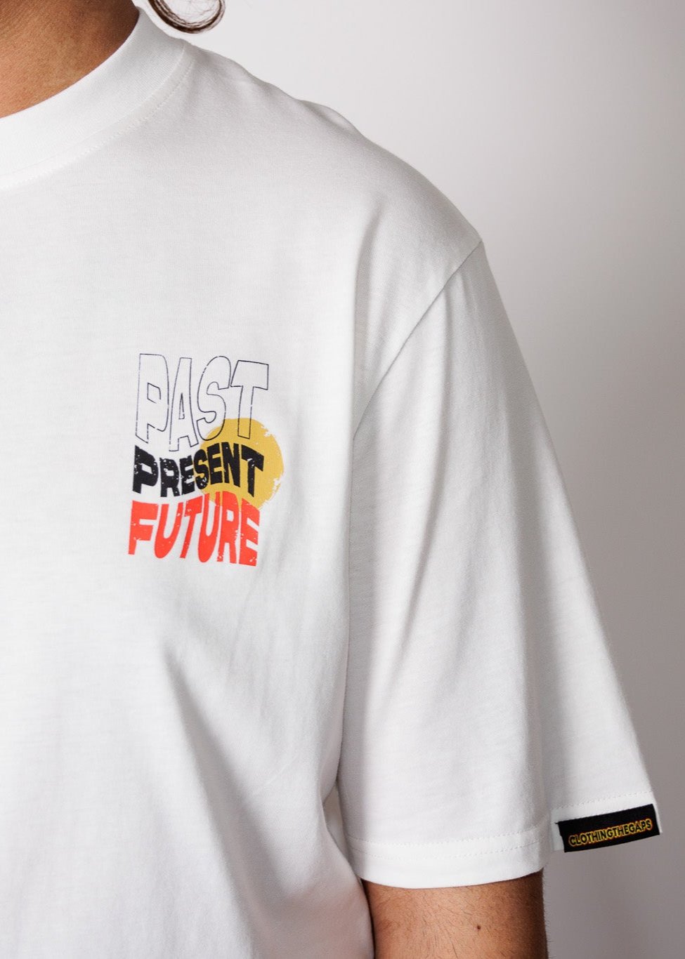 Clothing The Gaps. Past Present Future Tee. White tee with a small 'Past, Present, Future' pocket square on the front and large 'Past, Present , Future screen print back Black white and red with a yellow sun behind.