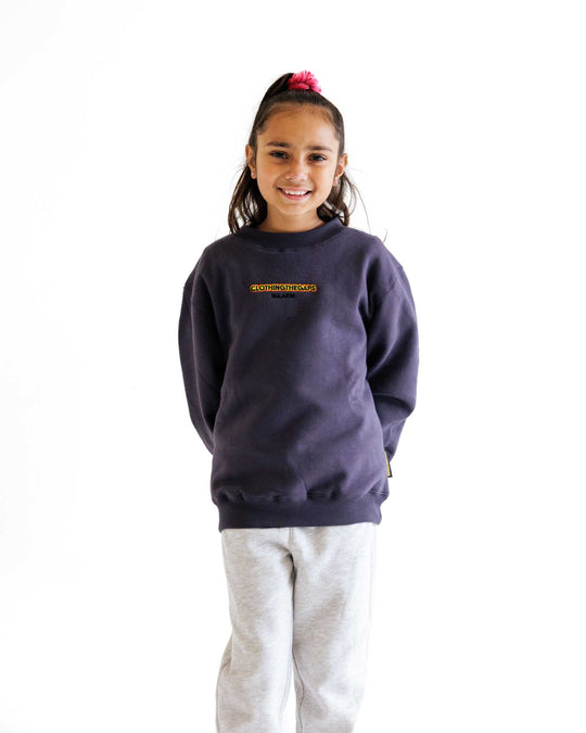 Clothing The Gaps. Kids Charcoal Crew Jumper. Charcoal dark grey crew neck jumper. With black, yellow and red 'Clothing the gaps' and the word 'Narrm' embroidered on the front of crewneck.' The wrist cuffs of the crew have a woven aboriginal flag on them. 