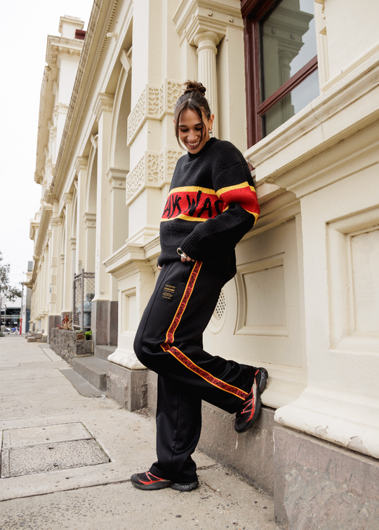 Person wearing a Clothing The Gaps black and red tracksuit leaning against a building.