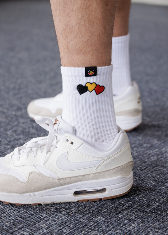 White Clothing The Gaps socks with colorful heart design worn with white sneakers on a gray floor.