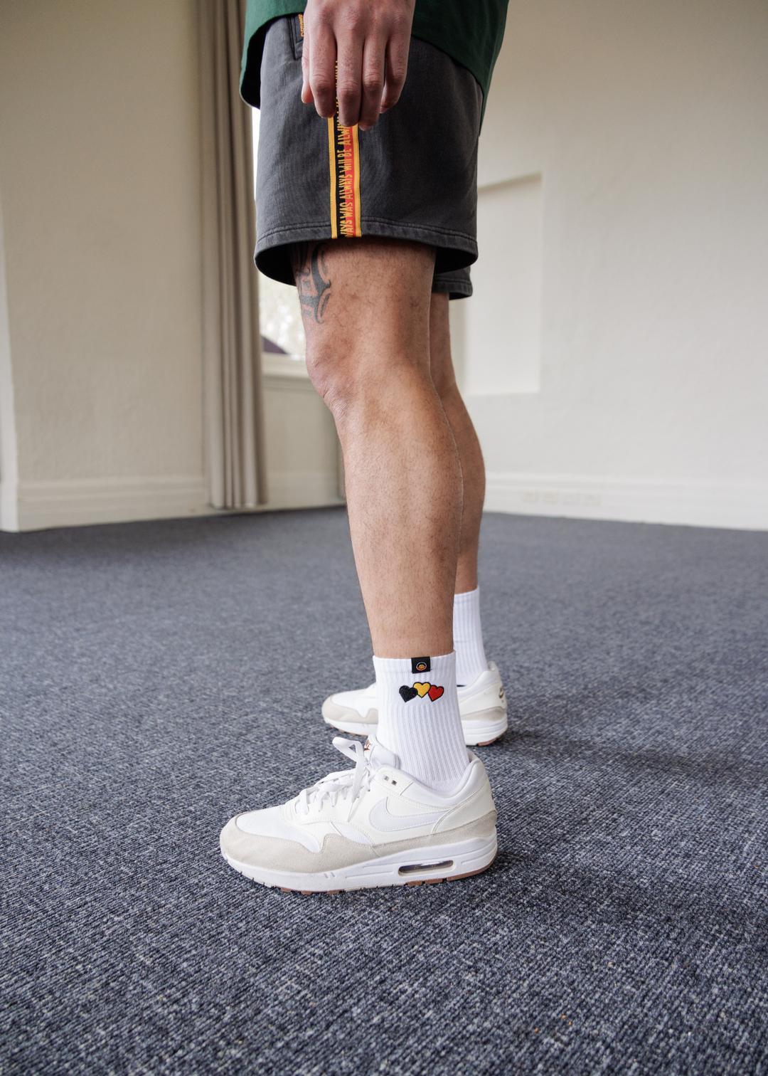 Person wearing white sneakers and clothing the gaps colorful socks on a carpeted floor.
