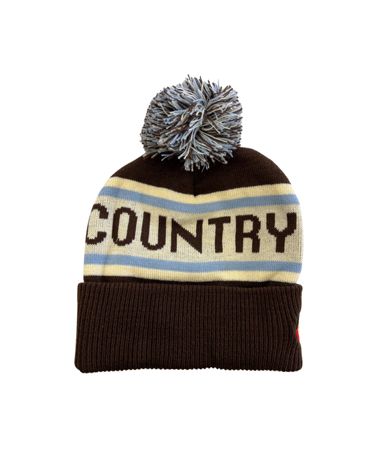 Clothing The Gaps. Honour Country Beanie. Chocolate brown base with thick butter cream middle section and two skinny ice blue lines above and below the chocolate brown text 'Honour Country.' Chocolate brown, butter cream and ice blue pom pom on top of beanie.