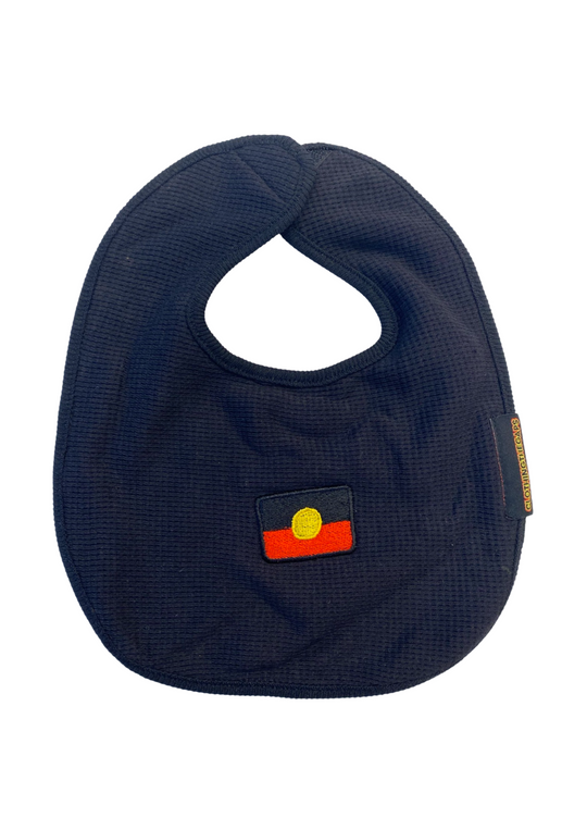 Clothing The Gaps. Flag Bubup Baby Bibs. Black bib cotton waffle material with red, black and yellow Aboriginal flag embroidered in centre. Includes Velcro to attach around babies neck.