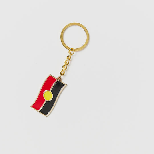 Clothing The Gaps. Keyring with gold chain and loop attached to Black, yellow and red aboriginal flag with skinny gold outline.
