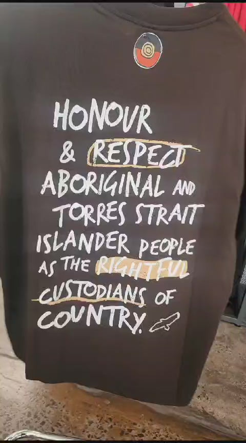 Clothing The Gaps. Handwritten Honour Country Tee. Expresso dark brown T-shirt with 'Honour Country' across chest in handwritten white text and coloured Aboriginal flag small underneath. On Back of tee white hand-writen style text 'Honour and respect Aboriginal and Torres Strait Islander people as the rightful custodians of country.' Circling 'respect' underlining 'custodians' and highlighting 'rightful' in a sand yellow colour. Outlined 'bunjil' eagle in bottom right corner.'    