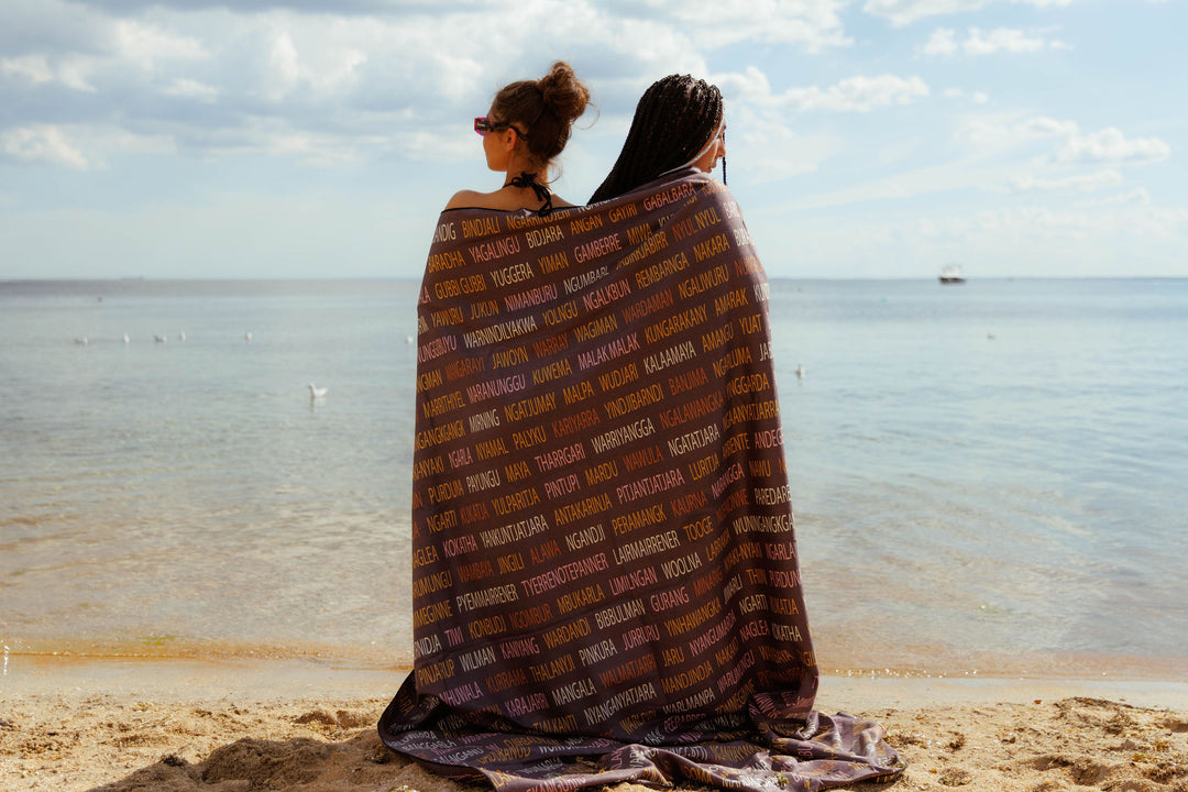 Clothing The Gaps. Gathering Blanket. Blanket is  extra large mob size. Made from premium Microfibre fabric.  Designed by Gunditjmara artist, Laura Thompson. Reversible blanket has a light grey background with light pink, maroon, light yellow and dark yellow alternating sections  inspired by traditional possum skin cloak and on the other side which has all Aboriginal language groups in same alternating colours.