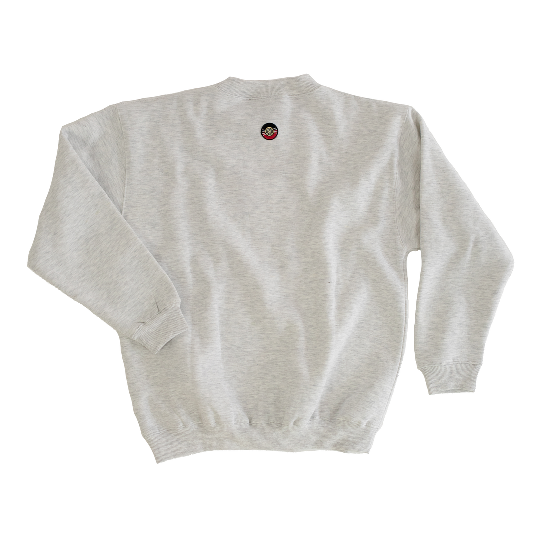 Clothing The Gaps. Classic Crew Jumper. This light grey crew jumper features a minimalist front embroidery piece proudly showcasing the words "Clothing The Gaps" in black with a yellow and red outline. Underneath a white embroidered outline in white of the Aboriginal flag.