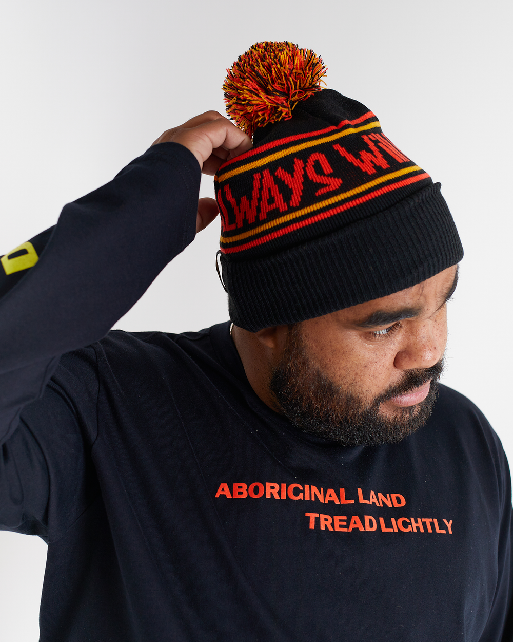 Clothing The Gaps. Power Beanie. Black base with two skinny red and yellow lines above and below bold capital red text 'Always was, Always will be.' Red, black and yellow pom on top of beanie. Embroidered clothing the gap.