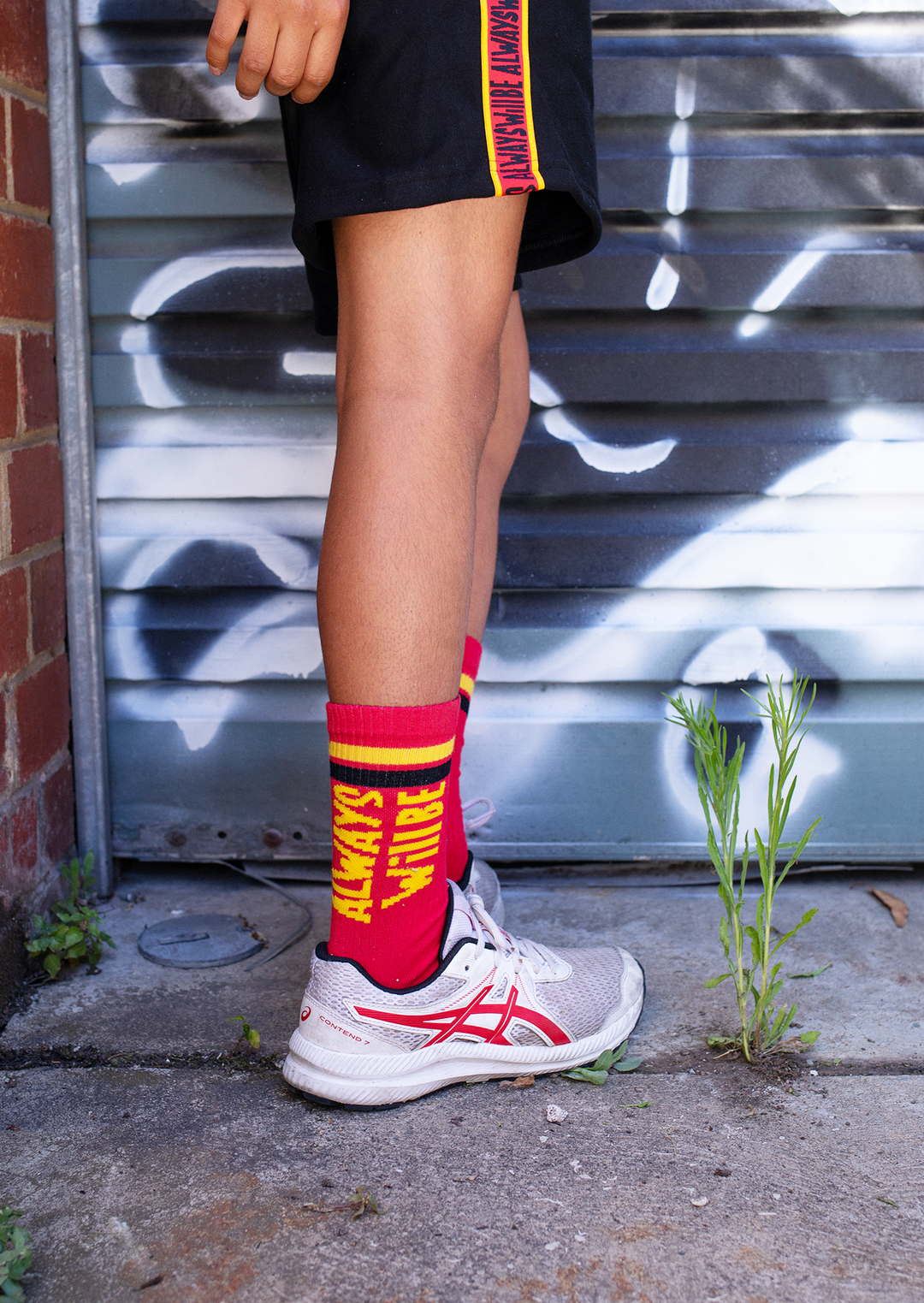 Clothing The Gaps. Power Socks 3 pack. 3 pack red, black and yellow thick cotton socks. Pair 1 Black base sock with 'Always was' on one side of sock and 'Always will be' on other side with red capital text and red and yellow band near top of sock. Pair 2 Red base sock with same text but in yellow and black. With yellow band near top of sock. Pair 3 yellow base sock with same text but in black. With black and red band near top of sock.