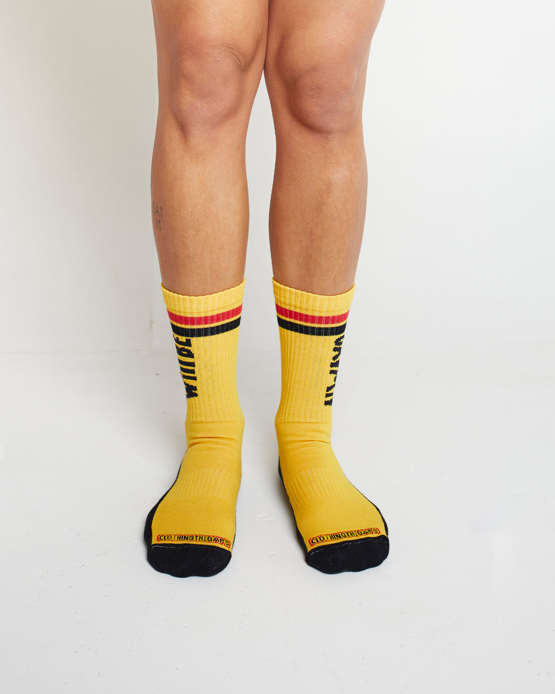 Clothing The Gaps. Power Socks 3 pack. 3 pack red, black and yellow thick cotton socks. Pair 1 Black base sock with 'Always was' on one side of sock and 'Always will be' on other side with red capital text and red and yellow band near top of sock. Pair 2 Red base sock with same text but in yellow and black. With yellow band near top of sock. Pair 3 yellow base sock with same text but in black. With black and red band near top of sock.