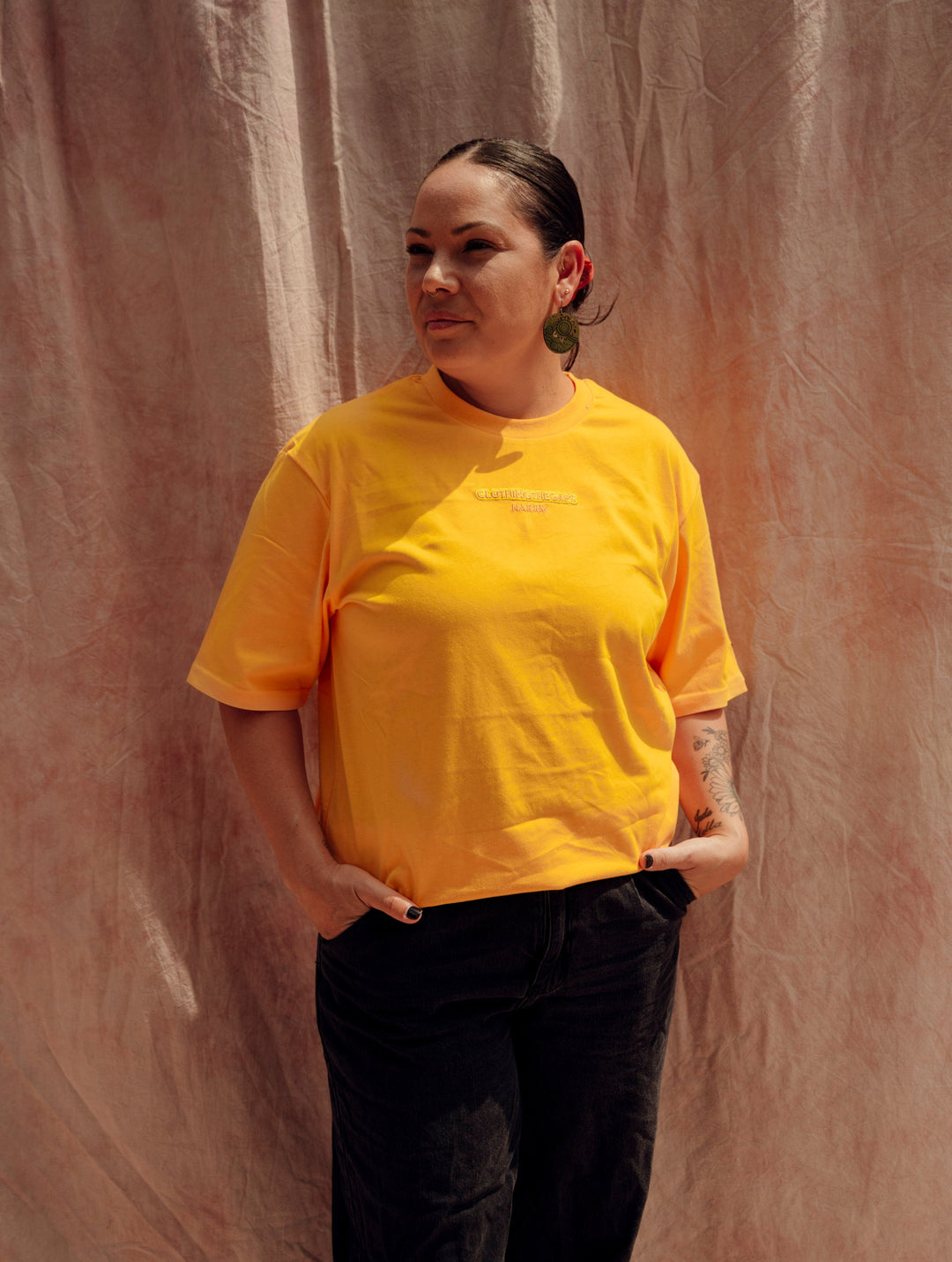 Clothing The Gaps. Sun Tee. Yellow T-shirt. With embroidered 'Clothing The Gaps' on front chest with minimalist font in a contrasting light yellow colour and 'Narrm' in a darker yellow embroidered underneath, acknowledging the land on which Clothing The Gaps operates it's social enterprise.