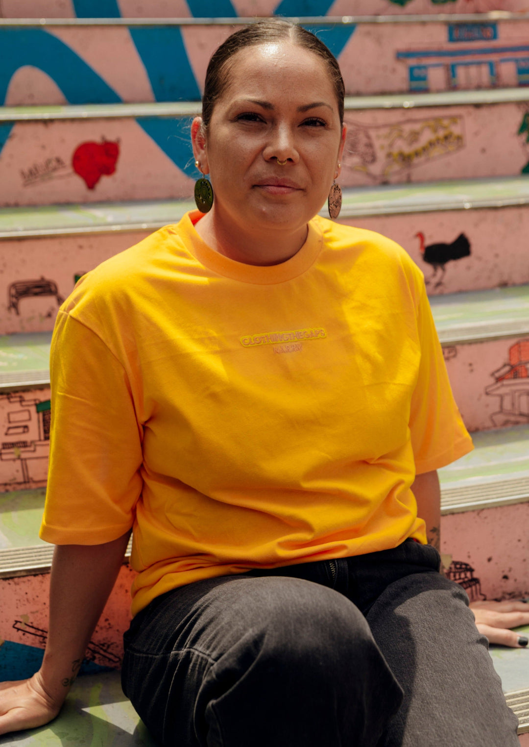 Clothing The Gaps. Sun Tee. Yellow T-shirt. With embroidered 'Clothing The Gaps' on front chest with minimalist font in a contrasting light yellow colour and 'Narrm' in a darker yellow embroidered underneath, acknowledging the land on which Clothing The Gaps operates it's social enterprise.