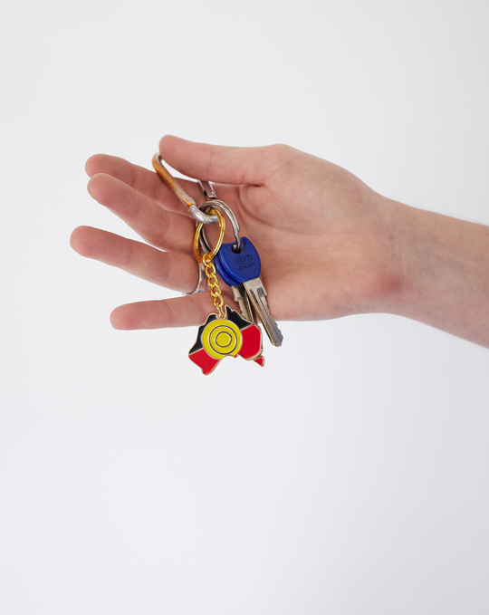 Clothing The Gaps. Keyring with gold chain and loop attached to black, yellow and red aboriginal flag colours shaped inside map of Australia with skinny gold outline.