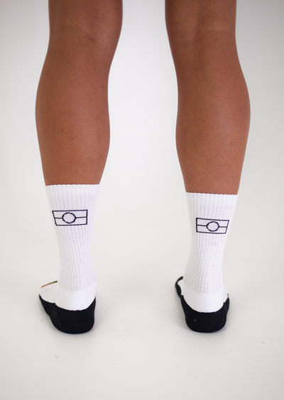 Clothing The Gaps. White Empty Flag Socks. Long white socks with black Aboriginal flag outline on back. Black on bottom of sock to hide dirt. Clothing The Gaps written above toe area.