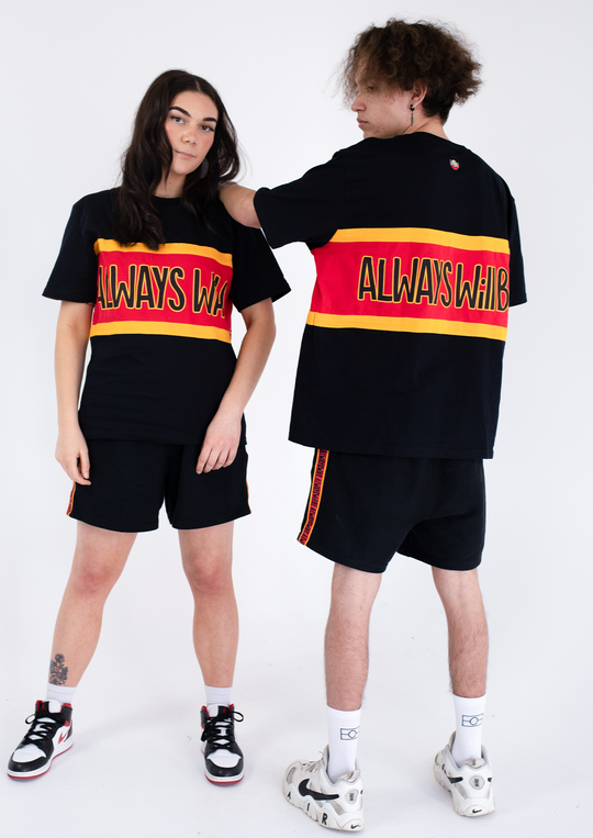 Clothing The Gaps. Power Rugby Tee. Red, black and yellow colorway. Black base tee with thick yellow top and bottom lines and red fill in mid section of jumper with big bold black text with a yellow outline in red section. Reading 'Always was' on front and on back in same text 'Always will be.' 