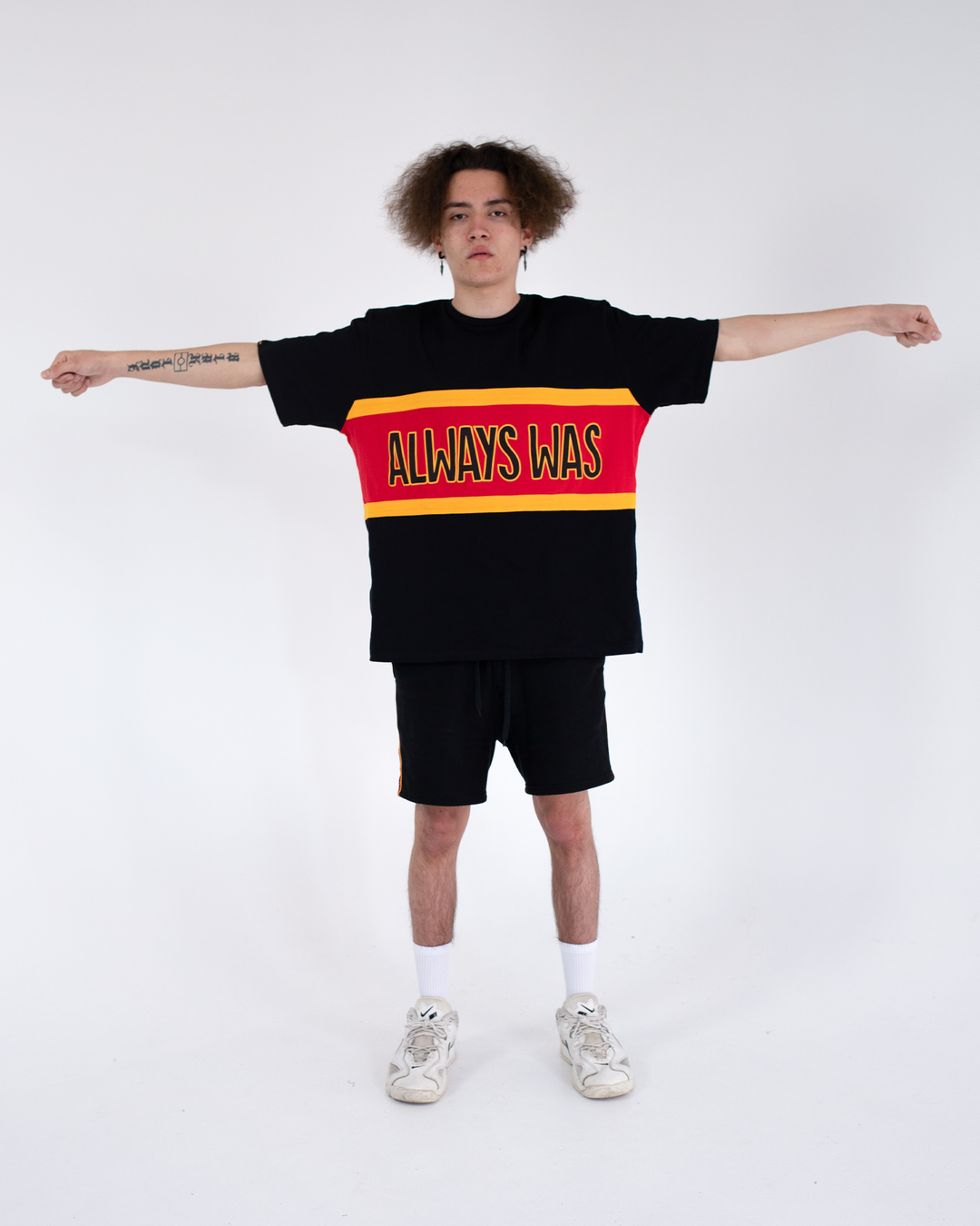 Clothing The Gaps. Power Rugby Tee. Red, black and yellow colorway. Black base tee with thick yellow top and bottom lines and red fill in mid section of jumper with big bold black text with a yellow outline in red section. Reading 'Always was' on front and on back in same text 'Always will be.' 