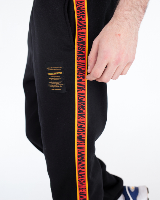 Clothing the Gaps. Black cotton Pants. With black drawstrings. Elastic cuts and waistband. Embroiled Clothing The Gaps logo. Black 'always was always will be' text on a red background with a yellow trim. In a cotton tape strip going down both sides of  pants.