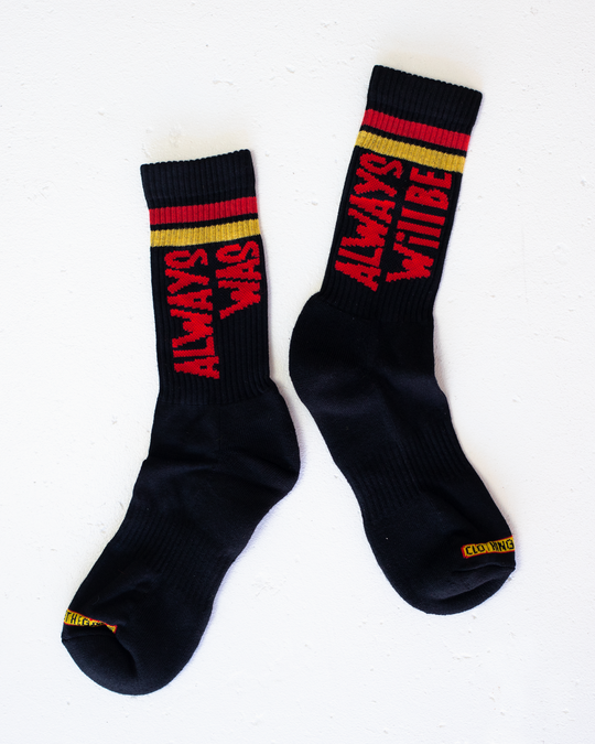 Clothing The Gaps. Power Socks 3 pack. 3 pack red, black and yellow thick cotton socks. Pair 1 Black base sock with 'Always was' on one side of sock and 'Always will be' on other side with red capital text and red and yellow band near top of sock. Pair 2 Red base sock with same text but in yellow and black. With yellow band near top of sock. Pair 3 yellow base sock with same text but in black. With black and red band near top of sock.