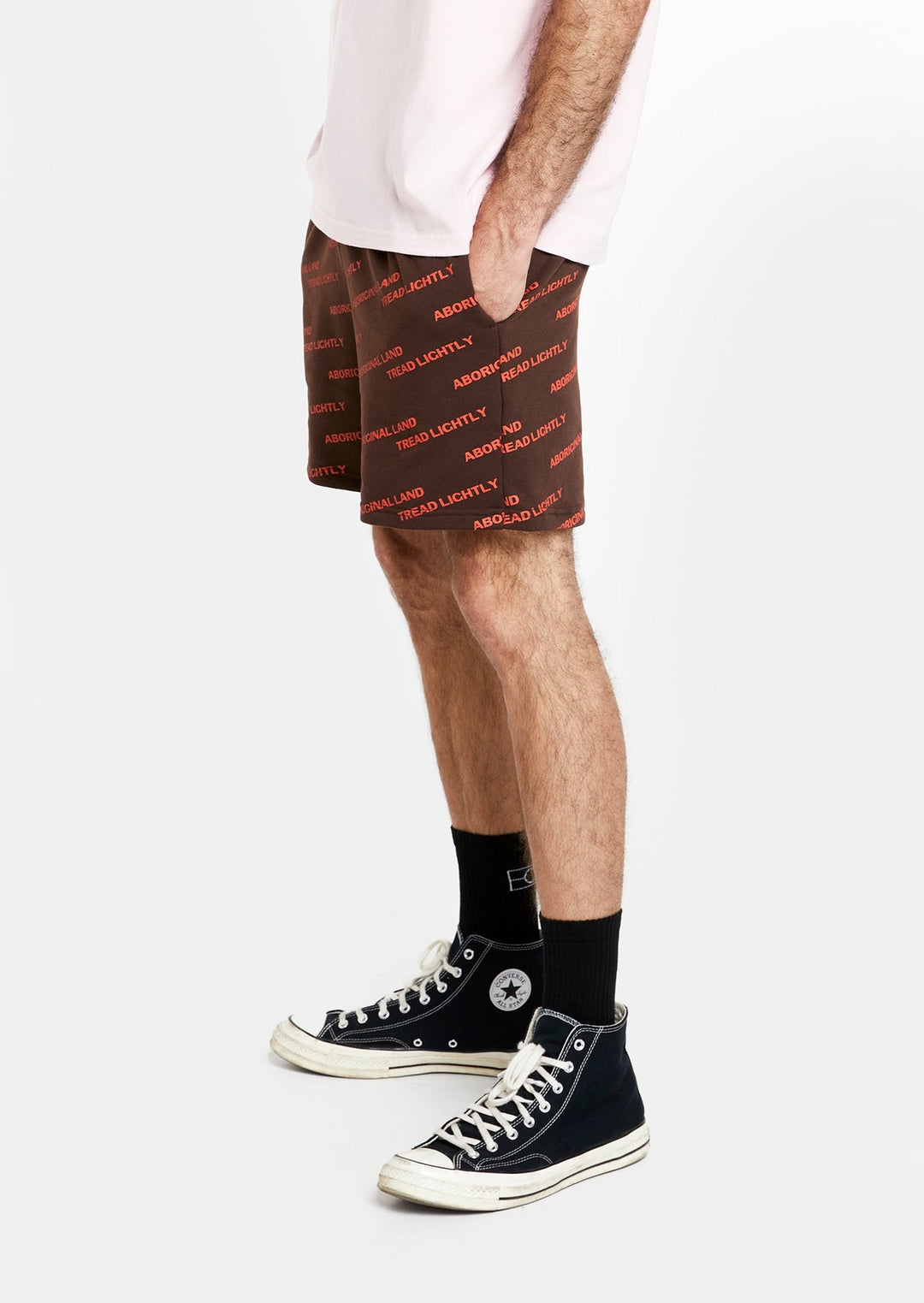 Clothing The Gaps. Orange Tread Lightly shorts. Brown shorts with repeating pattern all over crew of the words 'Aboriginal Land Tread Lightly' text in a orange colour. Includes solid brown elastic waist with brown drawstrings and has 2 deep pockets on both sides.