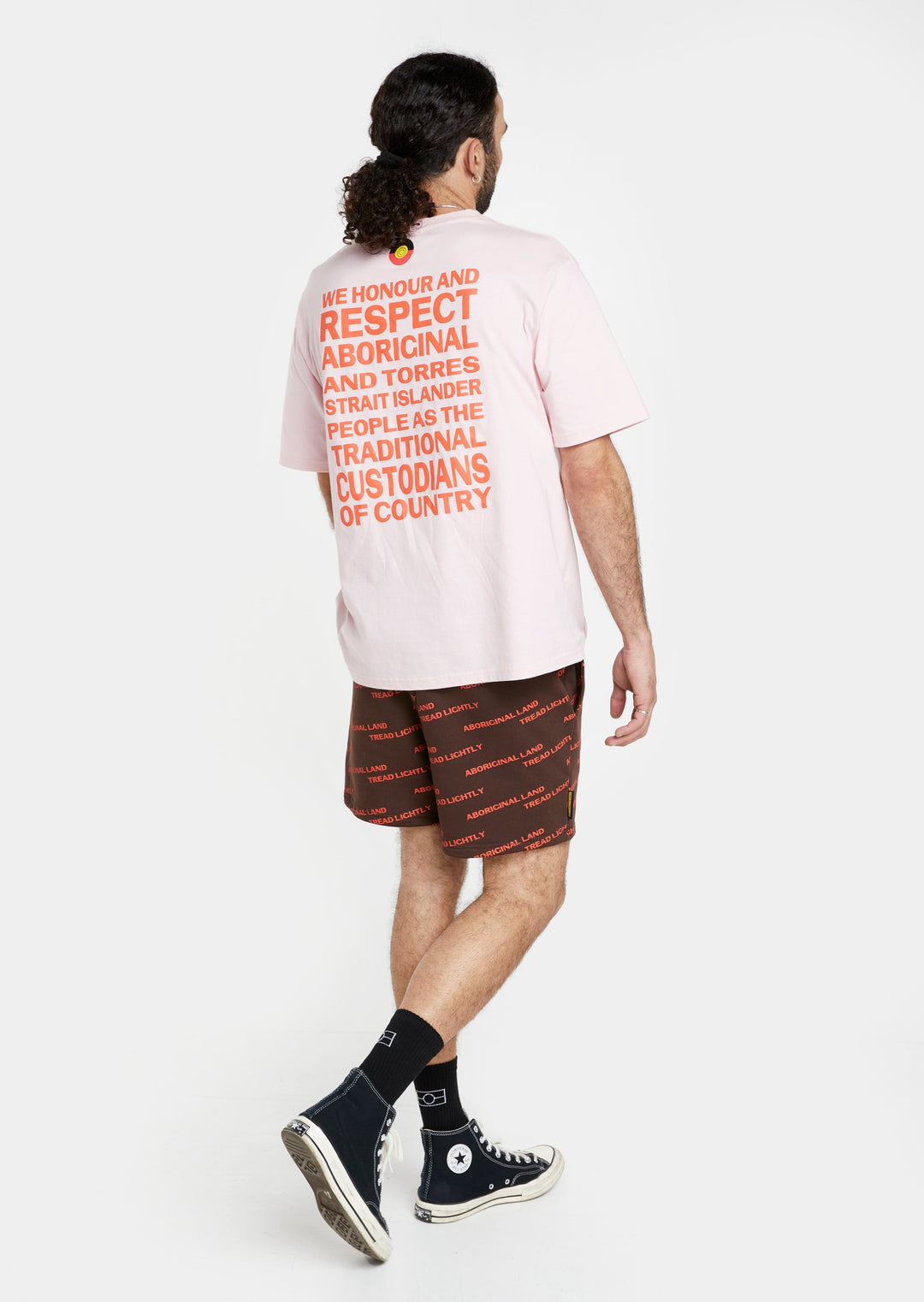 Clothing The Gaps. Orange Tread Lightly shorts. Brown shorts with repeating pattern all over crew of the words 'Aboriginal Land Tread Lightly' text in a orange colour. Includes solid brown elastic waist with brown drawstrings and has 2 deep pockets on both sides.