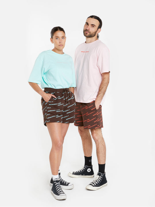 Clothing The Gaps. Blue Tread Lightly shorts. Brown shorts with repeating pattern all over crew of the words 'Aboriginal Land Tread Lightly' text in a light blue colour. Includes solid brown elastic waist with brown drawstrings and has 2 deep pockets on both sides.